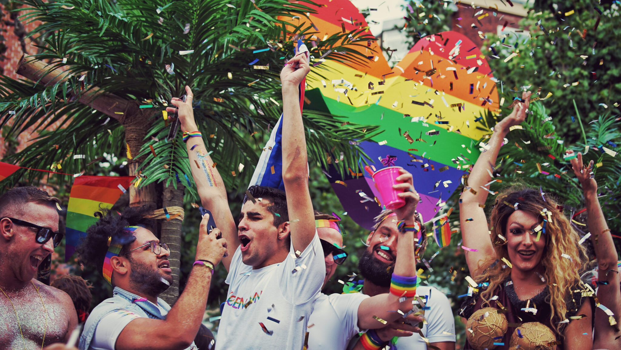 A person holding a rainbow flag with confetti raining down.